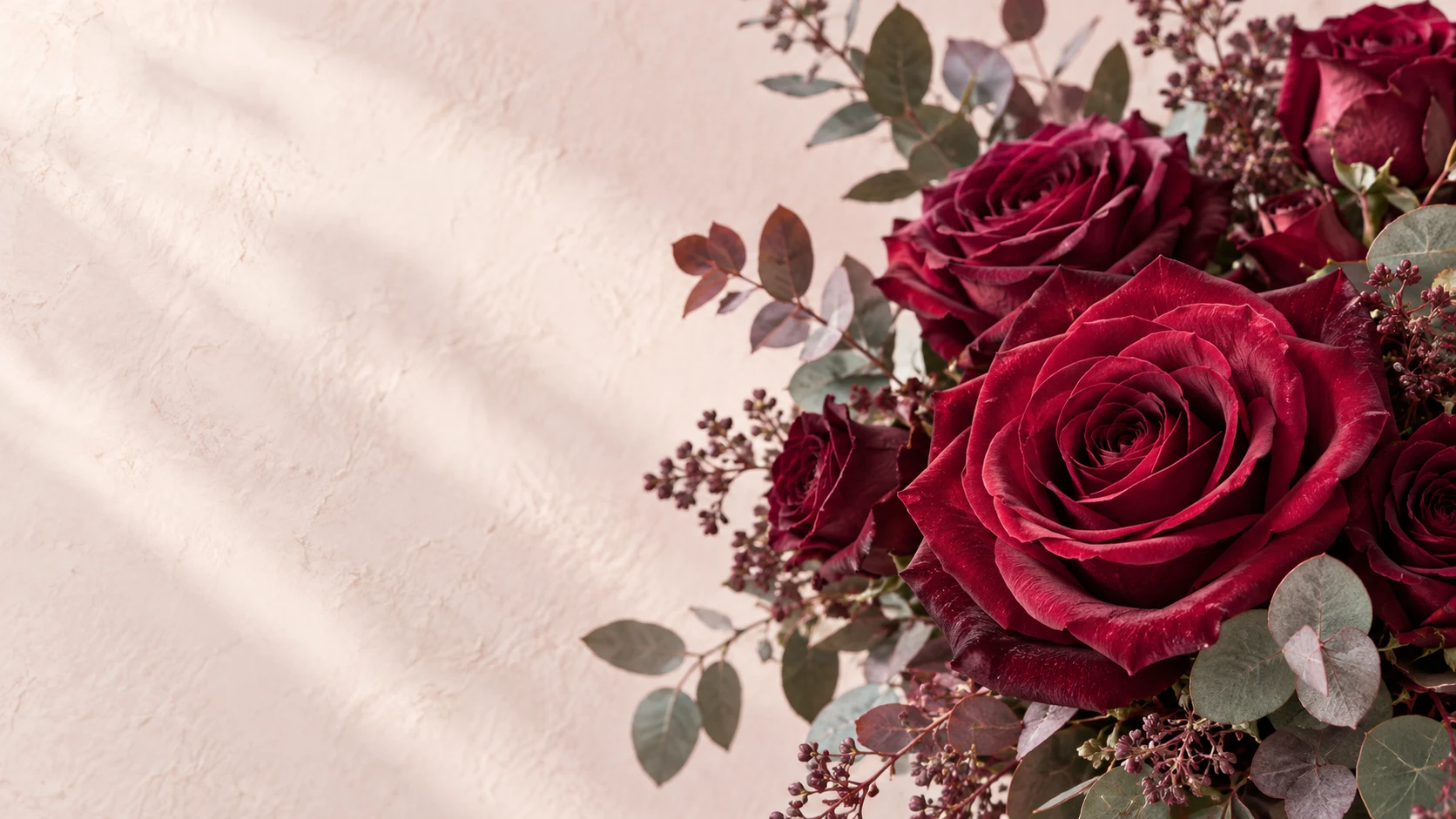 Roses bordeaux et eucalyptus sur fond minéral blush clair.